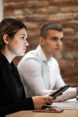 Two young professionals, a man and a woman, engage intently in a business meeting in an office with a rustic brick backdrop, portraying a modern professional environment.