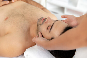 Caucasian man enjoying relaxing anti-stress head massage and pampering facial beauty skin recreation leisure in dayspa modern light ambient at luxury resort or hotel spa salon. Quiescent