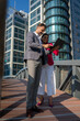 © Nenad - Smiling Latin Hispanic mature adult businesspeople using pc digital computer. Laughing caucasian colleagues, checking the company budget on their laptop in front of glass building exterior.