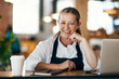 © HockleyM4/peopleimages.com - Woman, face and laptop in cafe for planning, catering service and recipe development with apron. Entrepreneur, portrait and smile in bakery for small business, online menu and management with startup