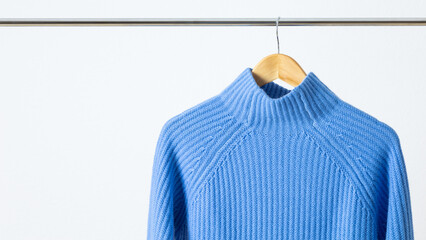 Soft casual sweaters of l blue luxury natural cashmere wool hanging on metallic hanger against white wall background. Autumn and winter pure wool clothing