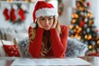 © Olena - Upset woman in Santa hat and red sweater sitting at table in front of bills against background of holiday decorations. Christmas stress