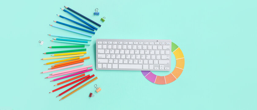 Workplace of graphic designer with PC keyboard, color charts and stationery on turquoise background, top view