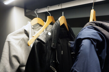 Modern wardrobe with wooden hanger and LED strip lighting. Hanging gray hoodie and leather jacket displayed. Sleek closet interior design with contemporary fashion pieces.