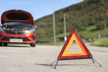 Close-up triangle emergency sign on the road, broken down car on the shoulder of the highway, warning of danger
