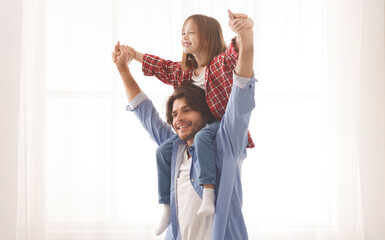 Wall Mural - Cheerful dad holding his happy little girl on shoulders, carrying her hands over white background, copy space