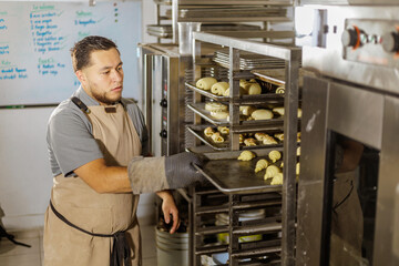 A focused Mexican baker aligns the trays of pan dulce in the bakery, ensuring they are perfectly positioned for baking, reflecting their dedication to quality and precision.