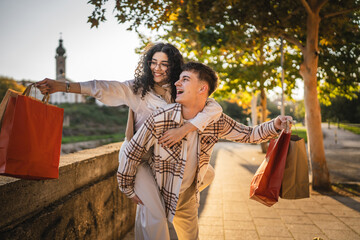 boyfriend hold girlfriend on his back while she holding shopping bags