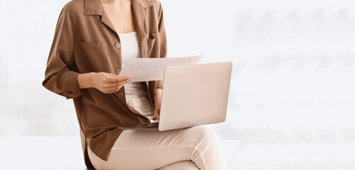 Poster - Office Worker. Cropped image of a girl sitting at office reading paper document with laptop on her lap, writing, copyspace