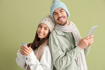 Poster - Loving couple in winter clothes using mobile phone and tablet computer on green background