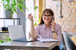 © Valerii Honcharuk - Portrait off middle-aged business woman working with laptop, talking on phone, sitting at desk