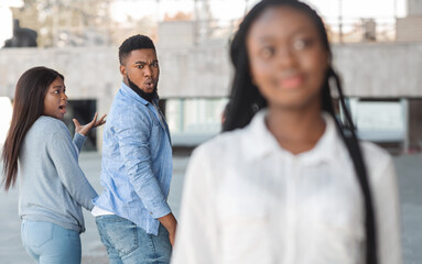 distracted african american guy turning around and looking to another woman while walking with his g