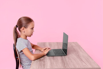 Wall Mural - Girl with correct posture using laptop at wooden desk on pink background