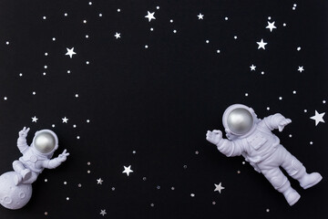 Astronaut toy figures on dark background decorated with star confetti. Selective focus, place for text