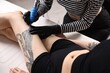 © New Africa - Professional artist tattooing woman's leg with machine in salon, closeup