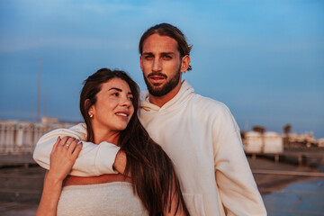 Beautiful young couple of fiancés hugging and exchanging gestures of love during a solitary outing to the sea at sunset	