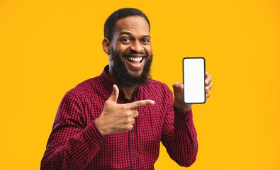 Poster - Smartphone Mock Up. Excited casual black man pointing at blank white cell phone screen, empty space, yellow studio