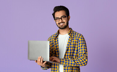 Poster - Happy Indian guy with laptop computer working or studying online on lilac background