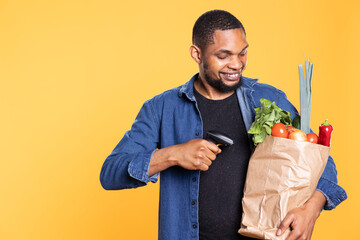 African american adult using scanner on organic produce in a bag, scanning natural bio groceries and recommending the local farmers market. Young person with zero waste veggies.