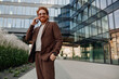 © Yaroslav Astakhov - A stylish businessman dressed in a suit is engaging in a phone call outside a contemporary glass office building
