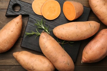 Wall Mural - Fresh raw sweet potatoes and rosemary on wooden table, top view