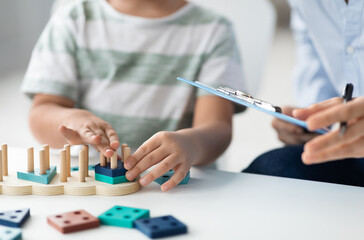 Kids development classes. Close up shot of unrecognizable little boy playing logical educational game during psychological consultation, specialist taking notes, empty space for text