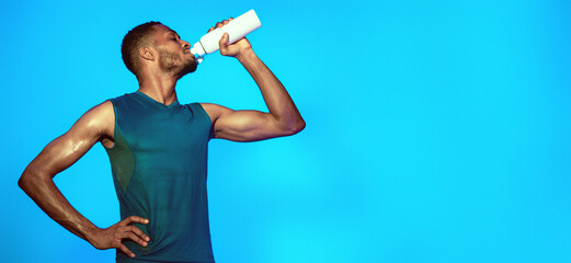 Workout Break. Black Sporty Guy Drinking Water After Exercising Over Blue Background In Studio.