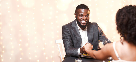 Happy black guy courting his woman, having date in fancy restaurant, man holding woman hand