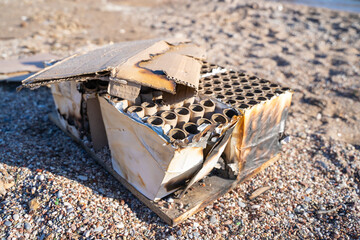 used firework box lies charred and discarded on a pebble-strewn beach, capturing the aftermath of a 