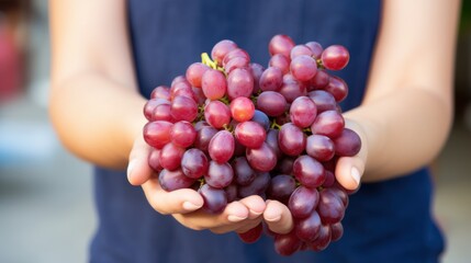 Plump red grapes rest in a woman's hands, showcasing their freshness and ripeness against a blurred background.