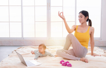 Asian mother workout after delivery newborn baby, young mom watching videos training lose weight yoga sport by computer laptop,  beautiful women and toddler infant play together with love and caring