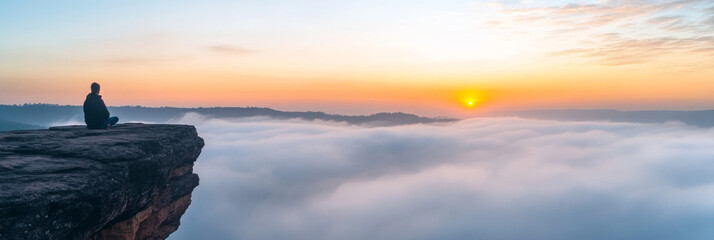 Wall Mural - Man sitting on a clifftop, watching the sunrise over a sea of clouds.