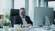 © pattozher - Zombie Boss: A humorously eerie image of a middle-aged man dressed as a zombie at work, sitting at his desk in a corporate office.