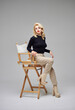 © SergeiPh - Beautiful girl with blond hair in a black sweater and brown pants posing in a studio on a gray background.