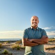 © Marc - Un hombre calvo, de aproximadamente 40 años, con una sonrisa amplia y una expresión de confianza. Está al aire libre, en un parque verde y soleado, con el cielo azul de fondo.
