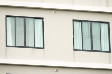 Two windows on a building with white walls and black frames. The windows are open and the curtains are drawn