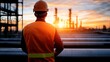 © Phirakhup - Worker in safety gear observing sunset at industrial site with pipelines.