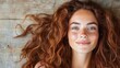 ©  Jovaduplex - A woman with beautiful curly red hair and freckles smiles brightly against a rustic wooden background, capturing a moment of natural beauty and happiness.