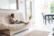 © Natallia - Boy sitting on a sofa holding remote control in hands. Child watching TV at home. Neutral colors. Scandinavian interior. Selective focus.