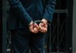 © Hanna - Businessman in handcuffs standing outdoors, arrested in a suit in an urban setting during daylight