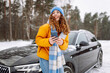 © maxbelchenko - Young woman with a phone near her car in a winter forest. Sending messages, communicating with friends. Technology, travel, lifestyle