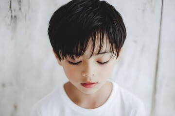 A serene asian boy closes his eyes, embodying calmness and introspection against a minimalist backdrop of light wood