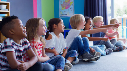 Wall Mural - Group Of Smiling Elementary School Pupils Sitting On Floor In A Line Listening To Teacher 