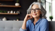 © halo - A middle-aged woman with gray hair and glasses sits on the sofa in her living room.