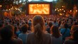 © Alienmarsh - A woman sits among a large crowd of people watching a movie on a large outdoor screen at an outdoor movie night.