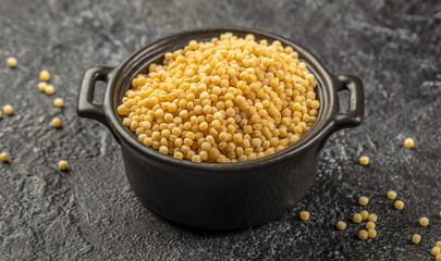 Raw ptitim pasta in a ceramic bowl on a dark background. top view