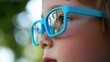 © Steve - Young child wearing blue glasses focusing on distant tree outside window, symbolizing myopia prevention and importance of outdoor activities.
