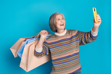 Wall Mural - Portrait of optimistic person dressed ornament pullover holding shopping bags make selfie on smartphone isolated on blue color background