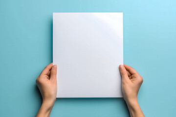 Female hands holding a blank white sheet of paper on a light blue background, ideal for showcasing designs, flyers, or invitations in clean and modern layouts