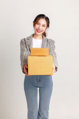 Smiling young Asian business owner woman leader entrepreneur wearing stylish suit holding parcel box for order shipping on isolated background.